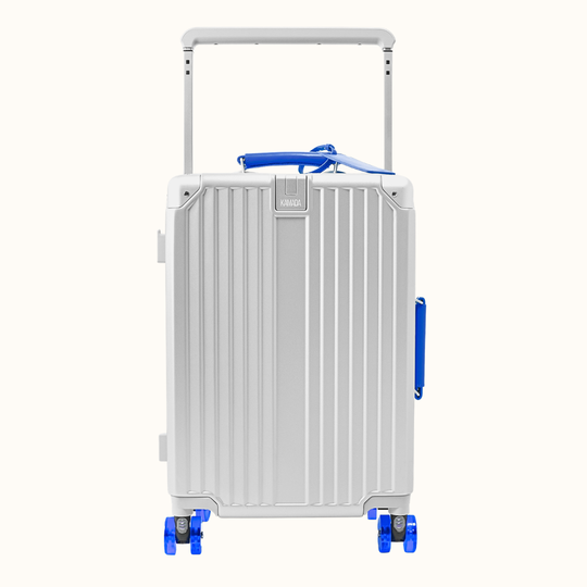 A silver aluminum hard-shell suitcase with vertical ribs, a telescoping handle extended, and bright blue accents on the top handle, side handle, and wheel areas, shown on a plain off-white background.
