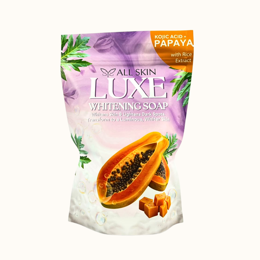 A stand-up pouch of All Skin Luxe White-Whitening Soap with Rice Extract, featuring purple and white packaging with illustrations of papaya and green leaves, on a light cream background.